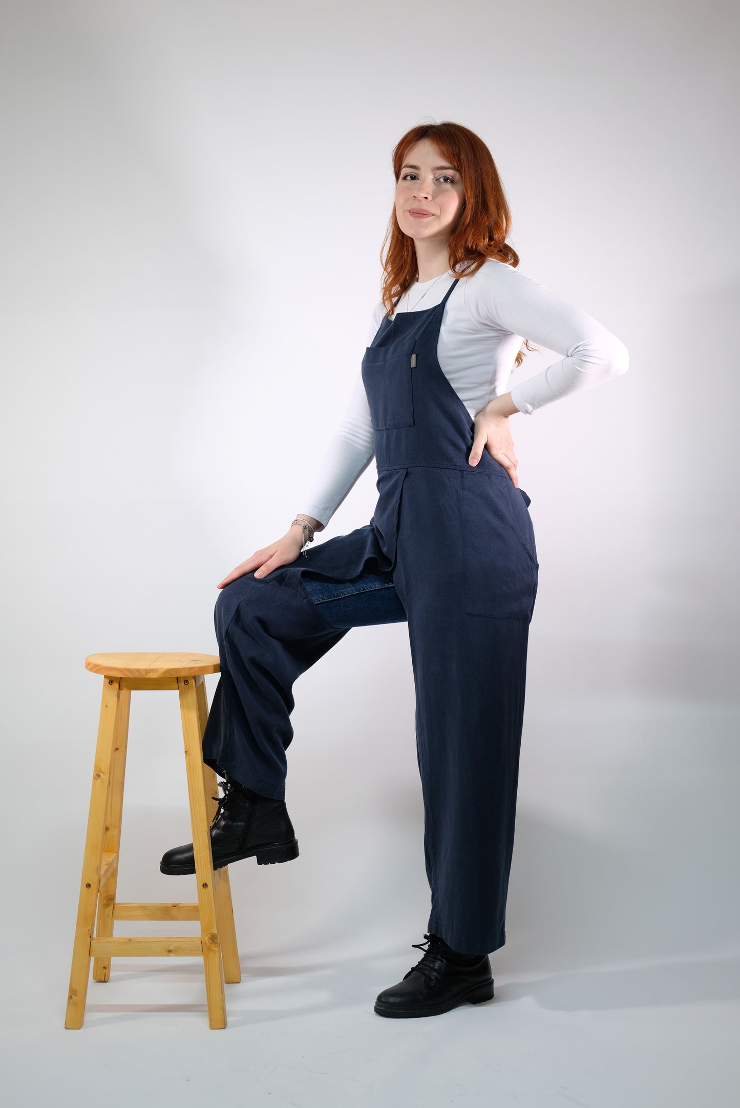 Artisan wearing navy split-leg jumpsuit apron at potter’s wheel.