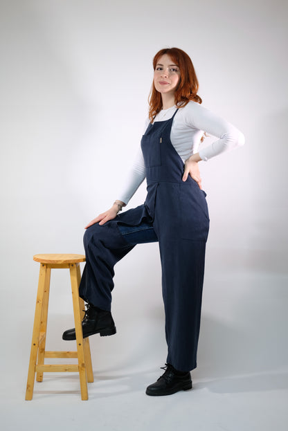 Artisan wearing navy split-leg jumpsuit apron at potter’s wheel.